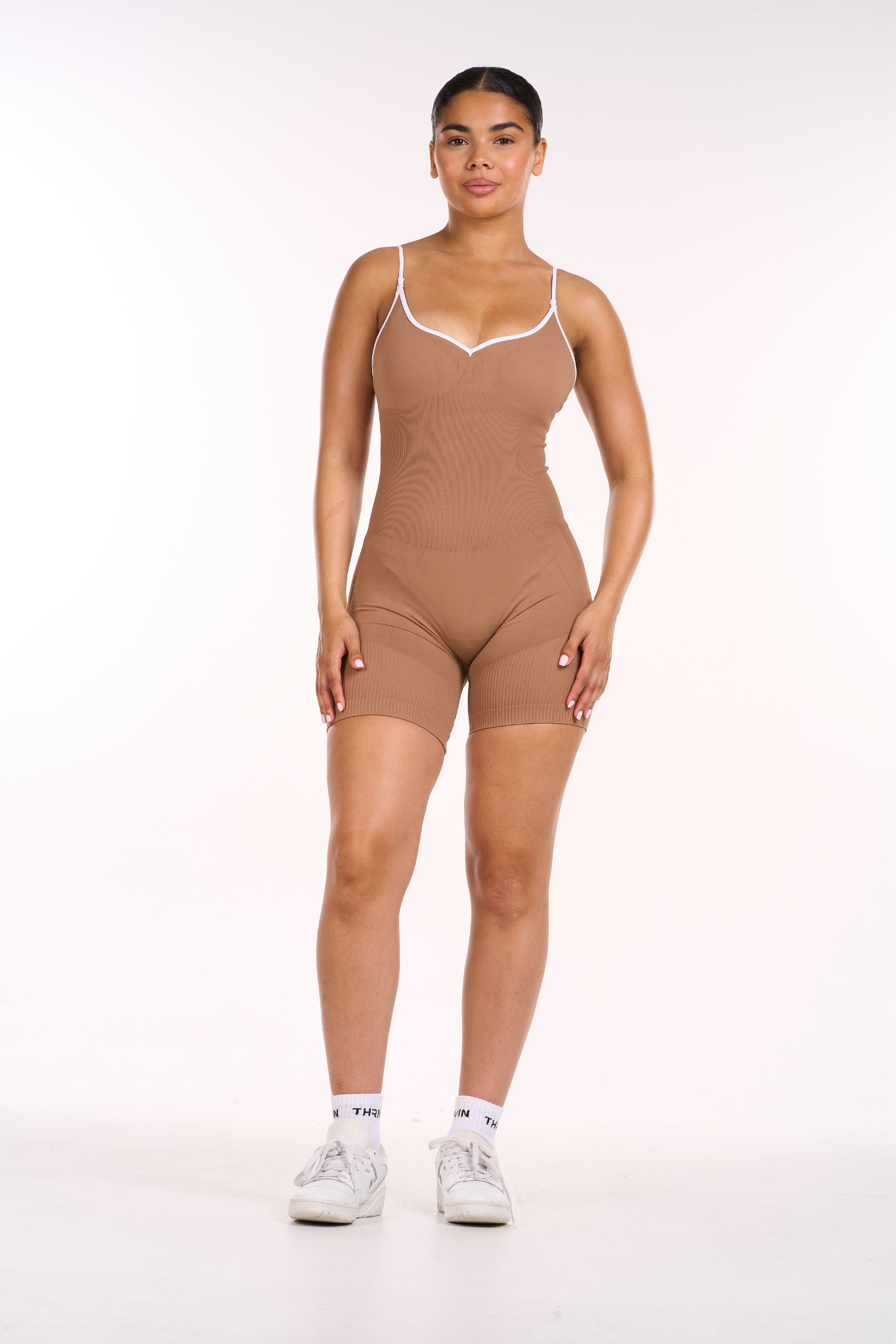 Woman wearing a brown bodysuit with thin straps on a white background